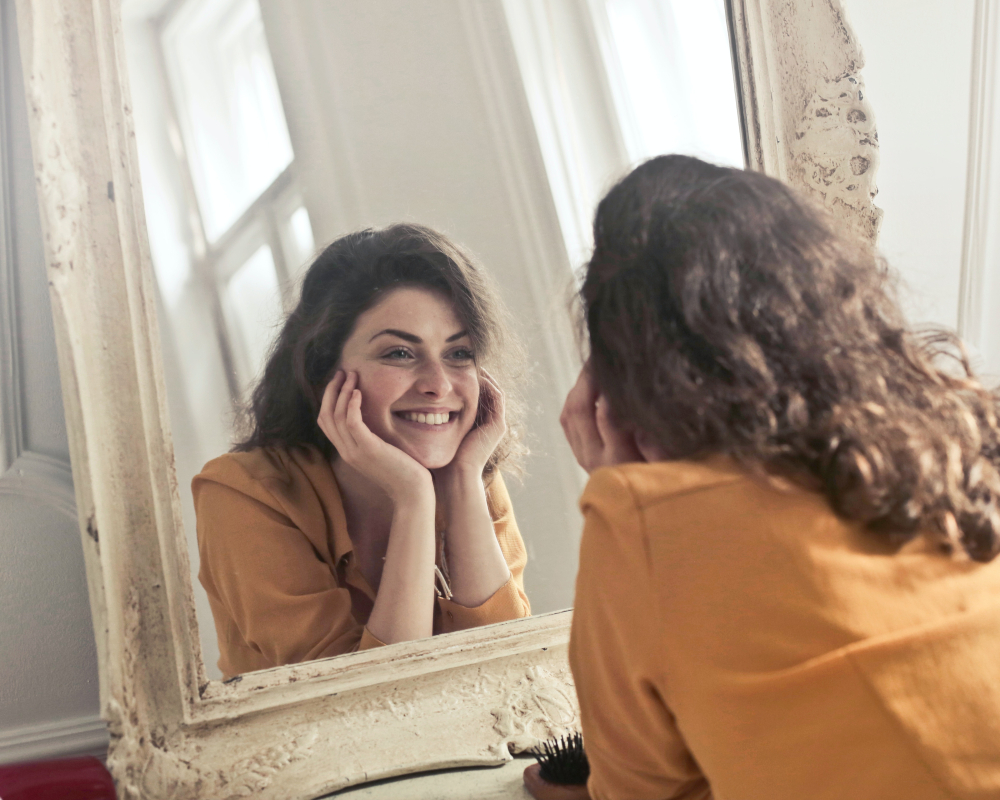 A woman smiling at herself in the mirror after finding happiness.