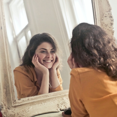 A woman smiling at herself in the mirror after finding happiness.