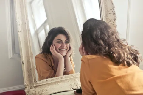 A woman smiling at herself in the mirror after finding happiness.