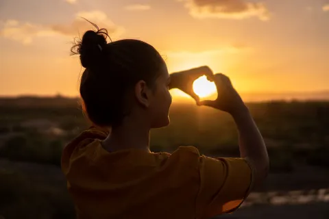 A woman is doing a heart sign towards the sign.